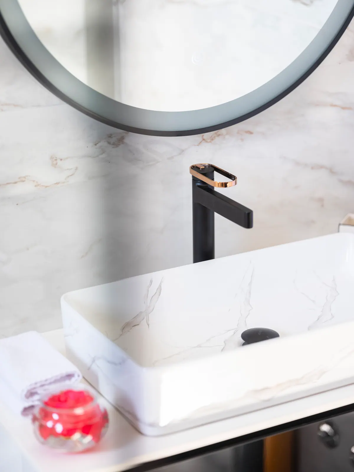 A marble basin with a black tap under a round mirror