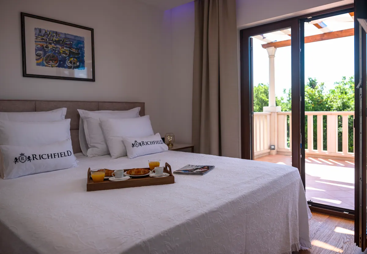 A bedroom with breakfast on the bed and the balcony door open