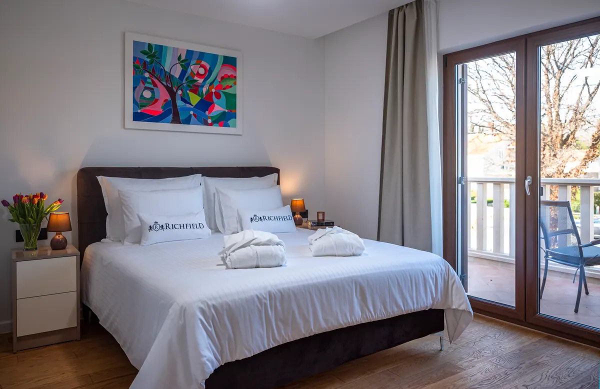 A king-size bedroom with a balcony door and white linen
