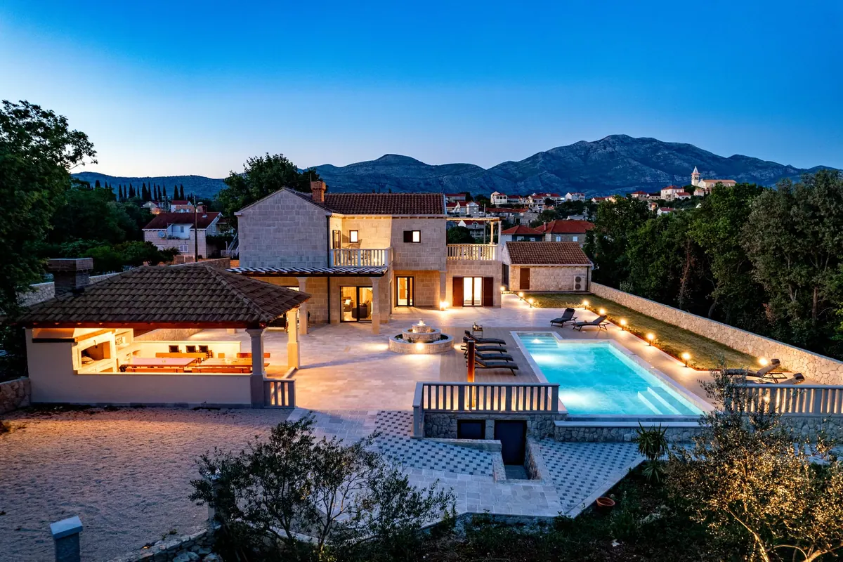 The pool at dusk, lit from below, with the villa and the mountains behind