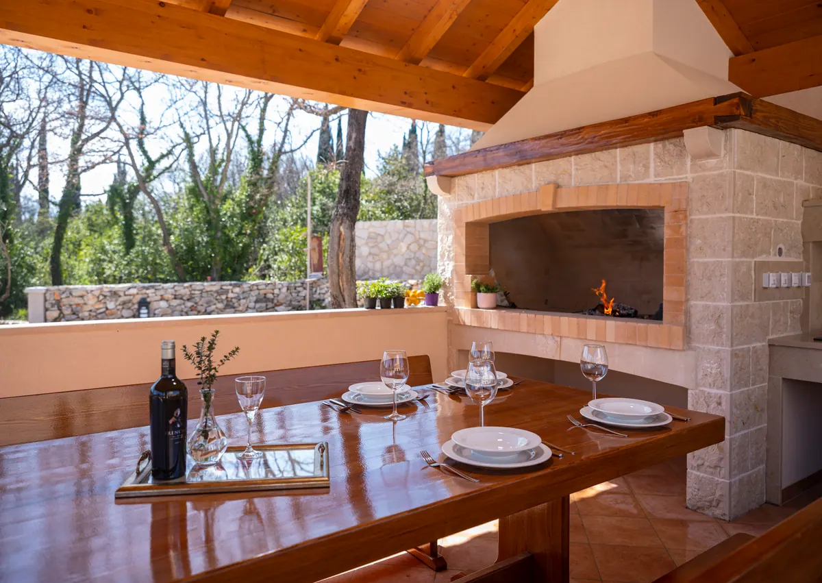 The outdoor kitchen with a brick-built barbecue and a long wooden dining table
