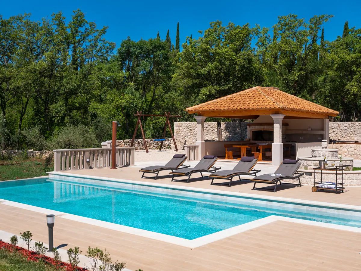 The pool, sun loungers and the tiled pavilion with the outdoor kitchen