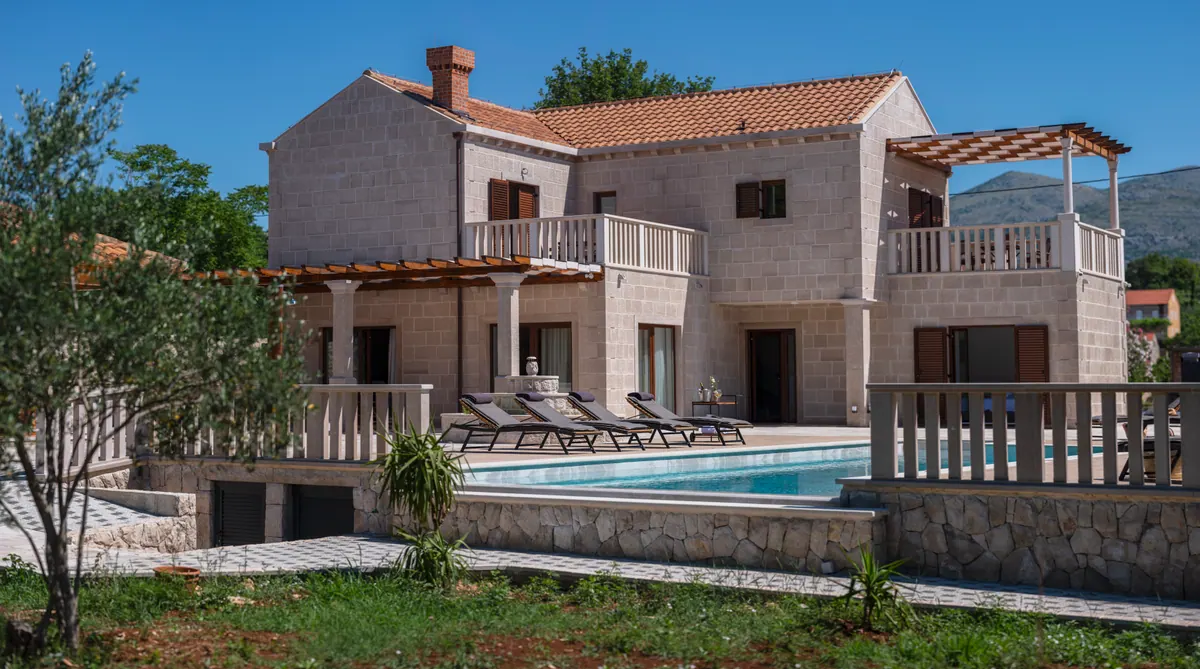 Villa Peleo from the garden: a two-storey stone house with balconies, a pergola and the pool terrace